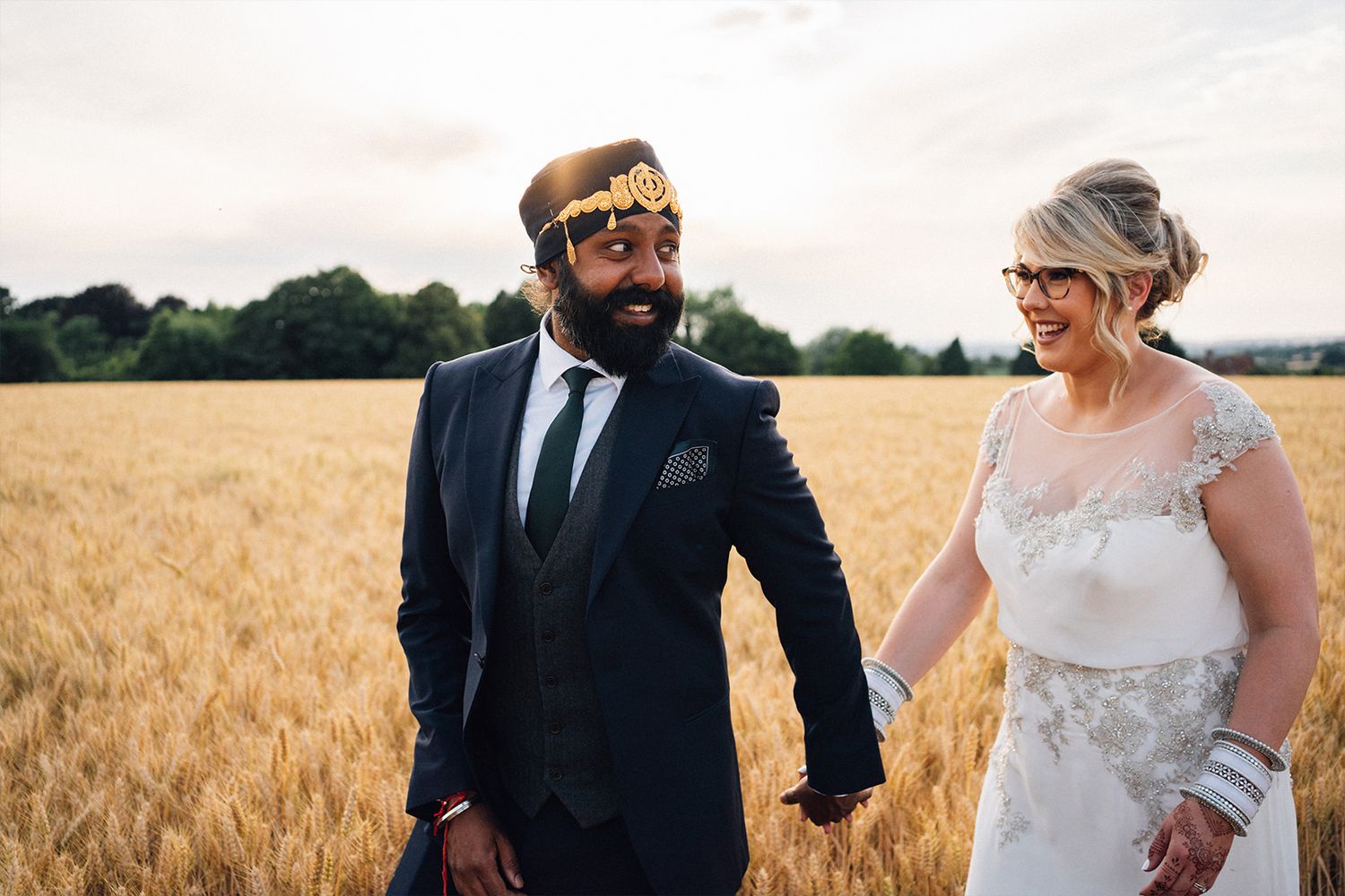 A couple in wedding attire holds hands while standing in a golden wheat field on their special day.