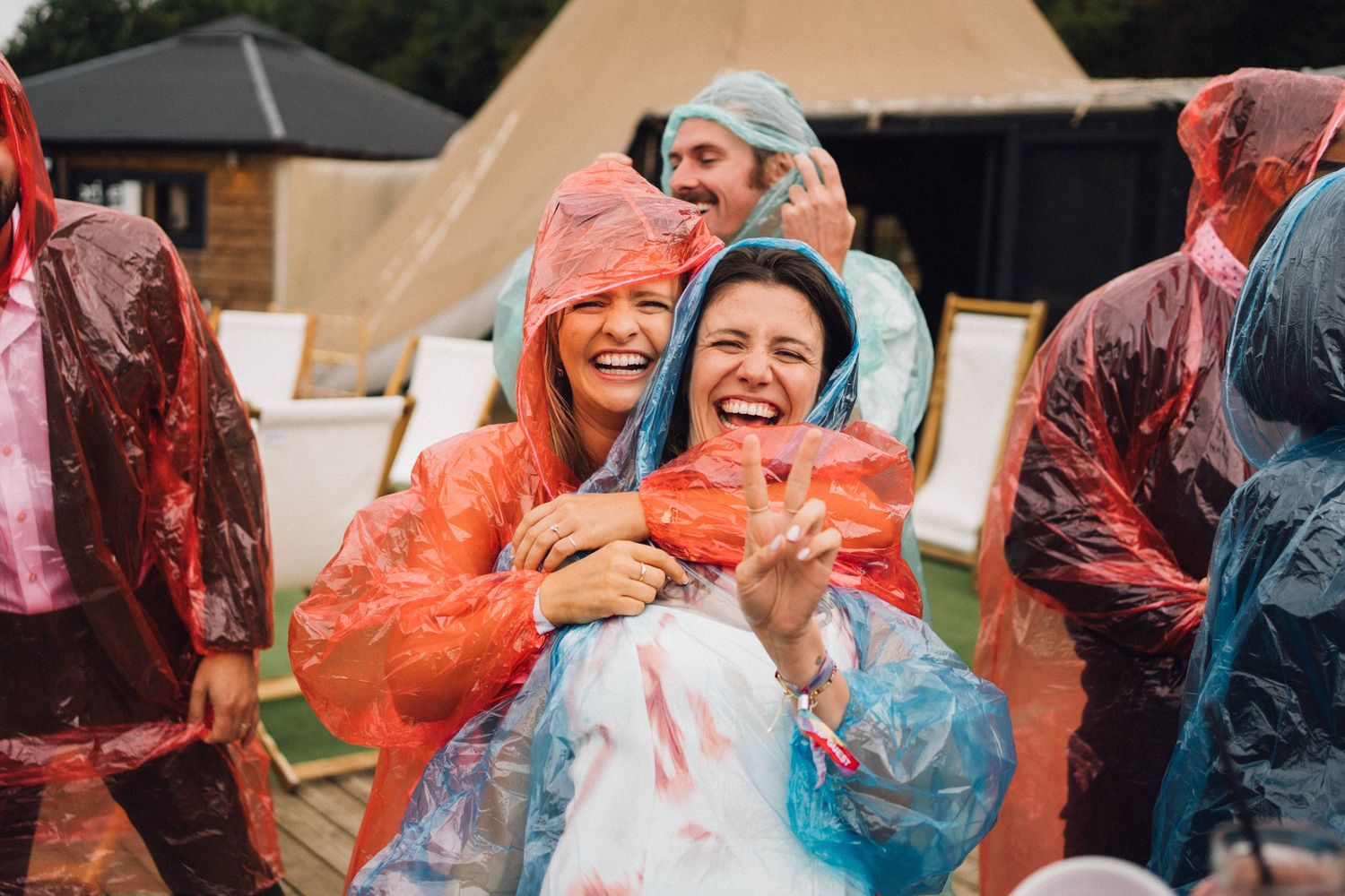 People wearing colorful rain ponchos laugh and embrace during a rainy outdoor event.