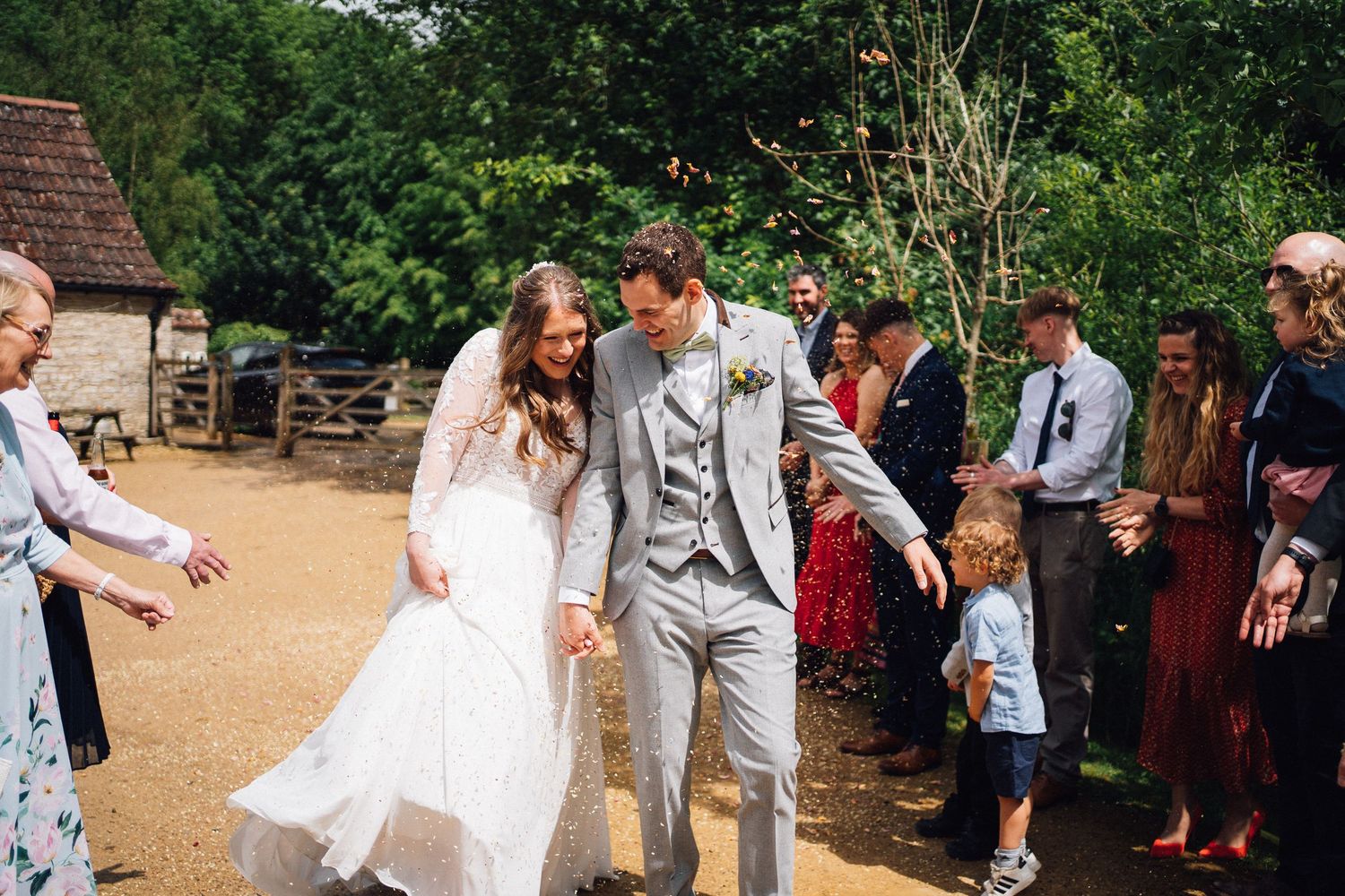 Wedding party celebrates outdoors on a sunny day surrounded by trees and guests.