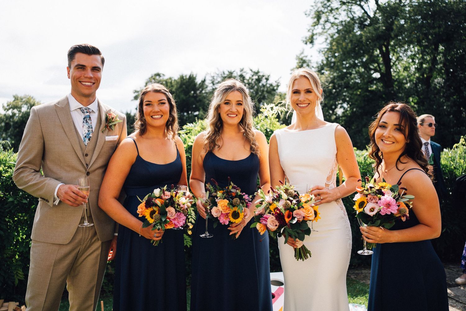 Wedding party poses for formal photos in garden with colorful bouquets.
