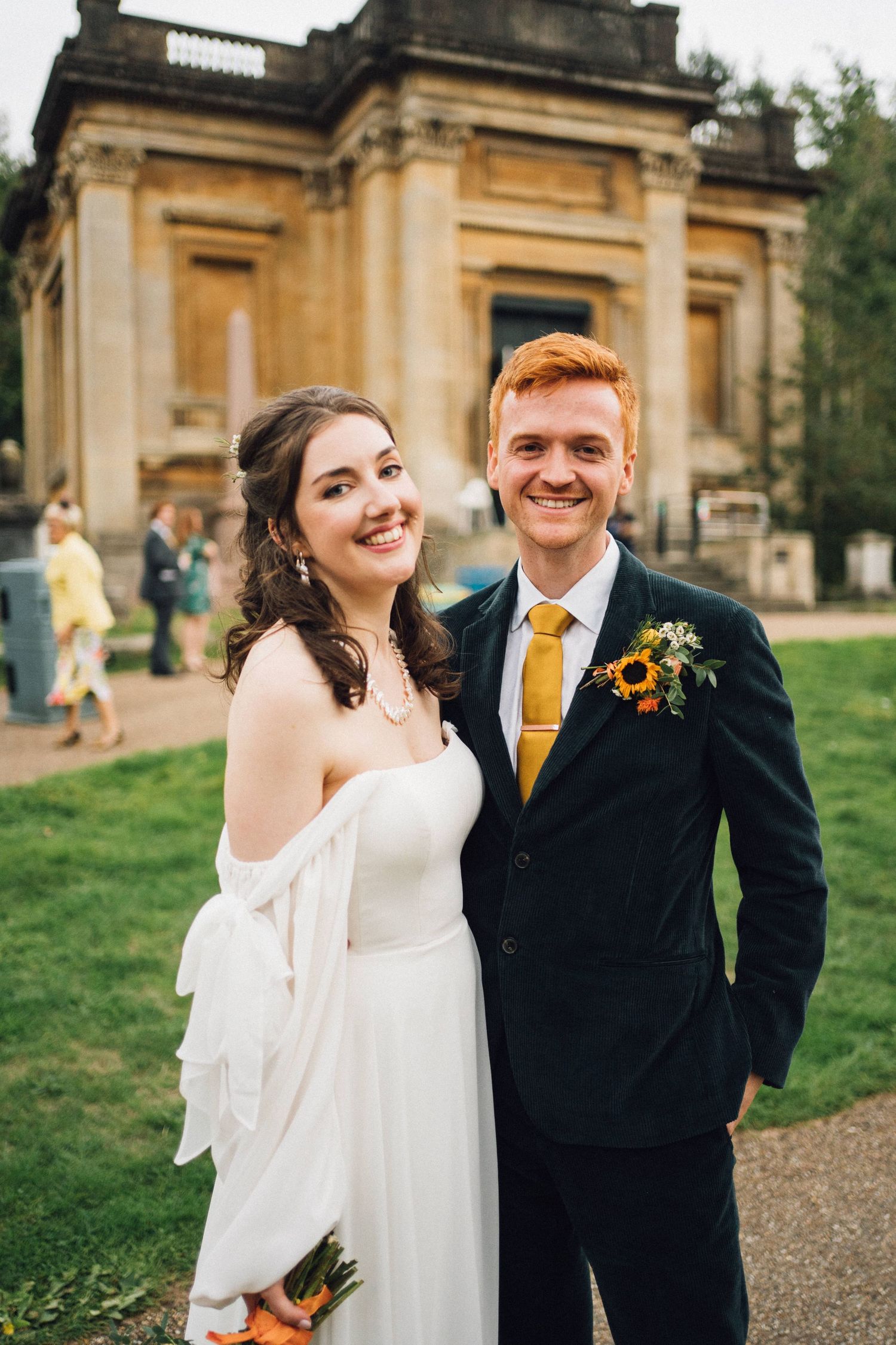 A couple poses in front of a historic sandstone building on their wedding day.