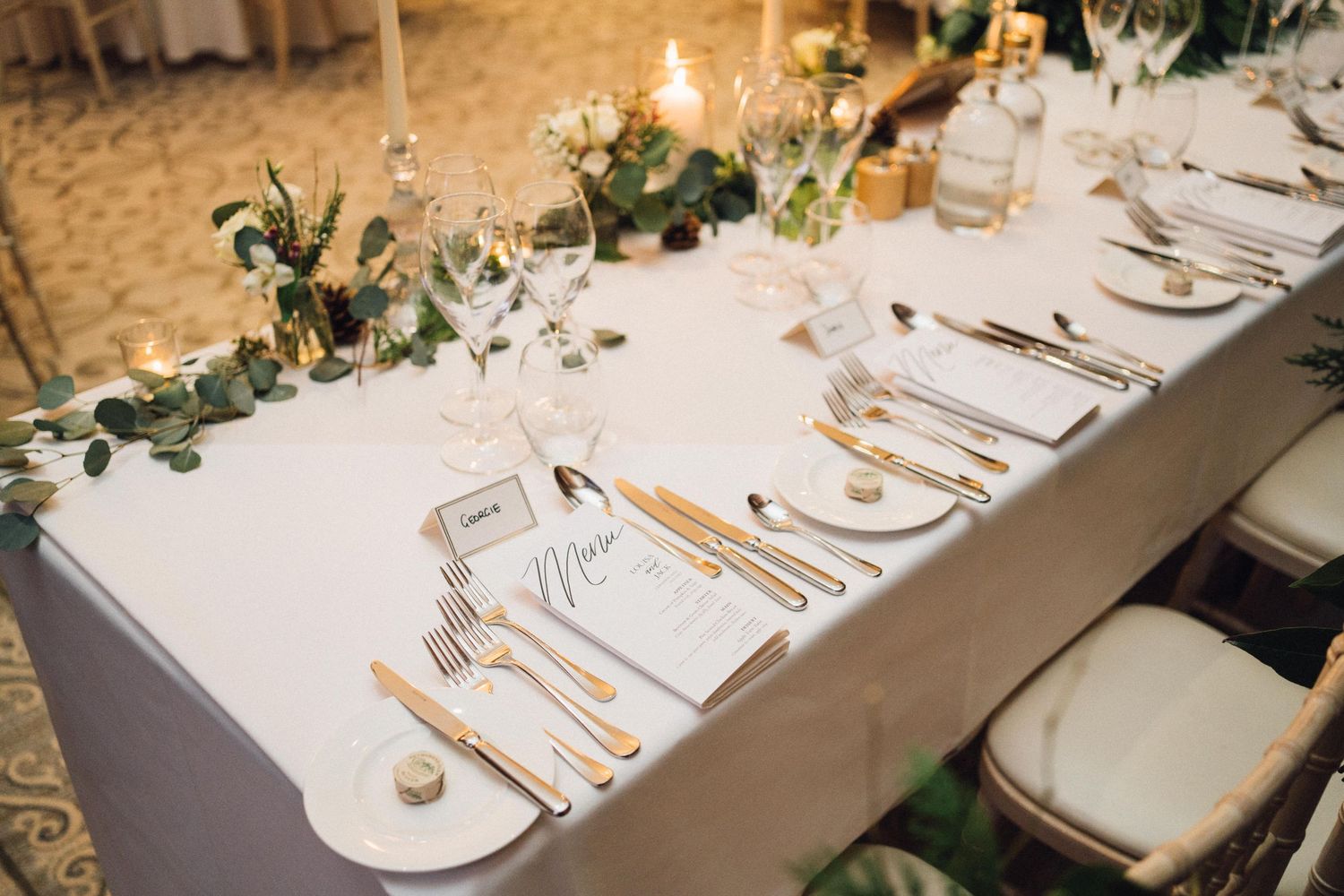 Candlelit wedding reception table with elegant place settings and greenery accents.