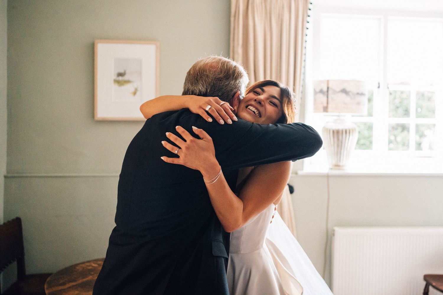 Two people share an emotional embrace, one wearing a white wedding dress and the other in dark formal attire.