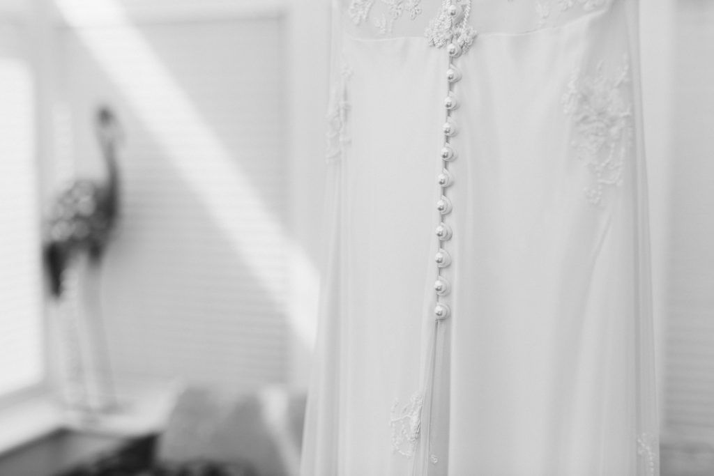 Close-up of delicate white wedding dress details hanging in natural window light.