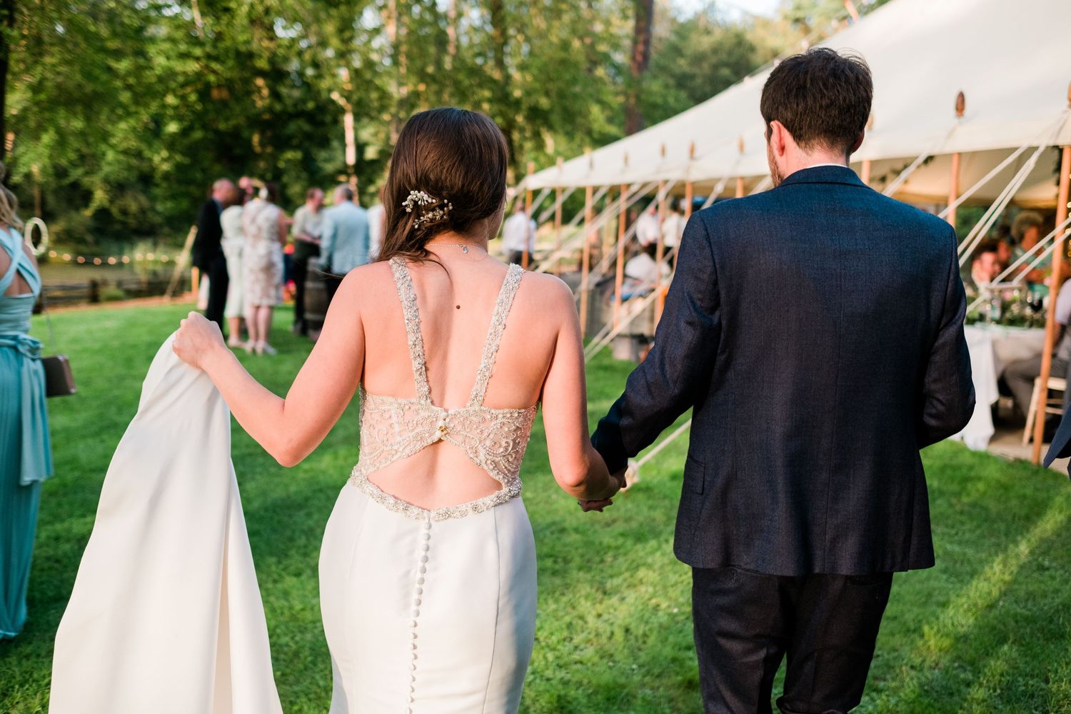 Guests walk across a lush green lawn towards a white wedding reception tent at dusk.
