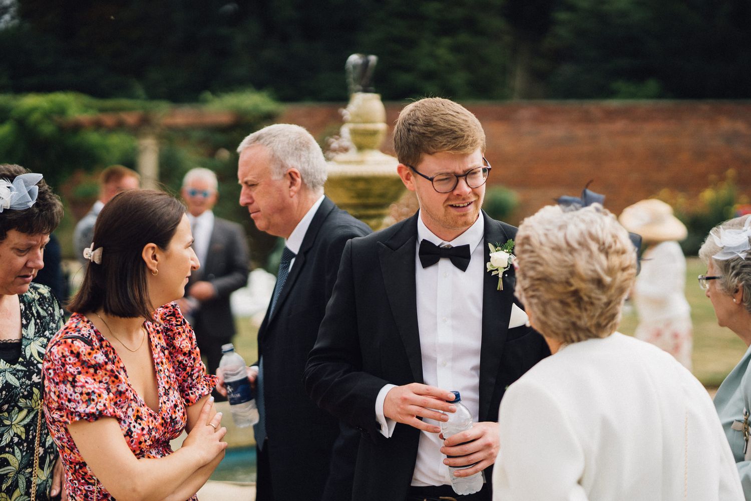 Elegant outdoor wedding reception with guests gathered on a lawn near historic brick walls.
