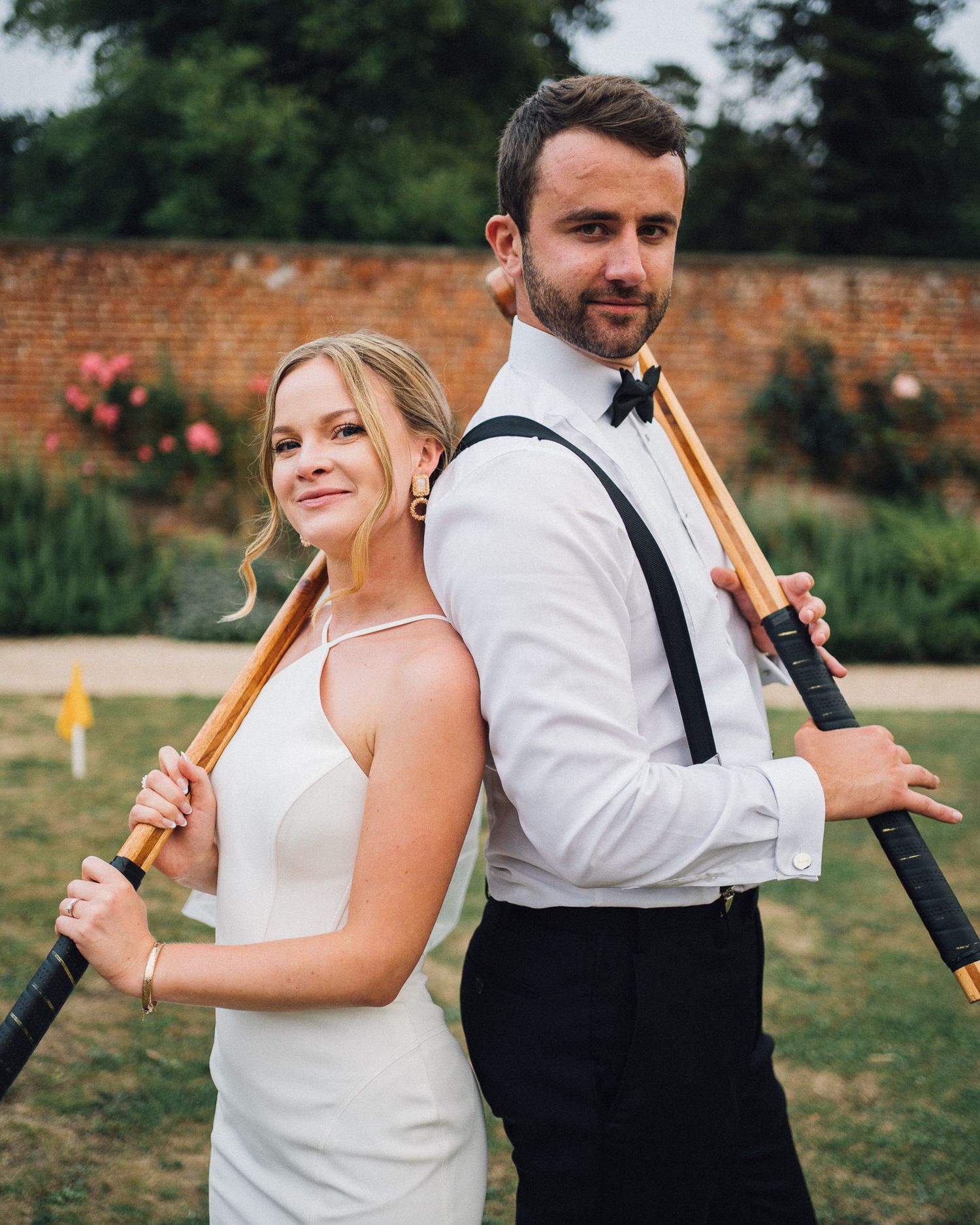 A couple in wedding attire poses back-to-back with playful expressions.