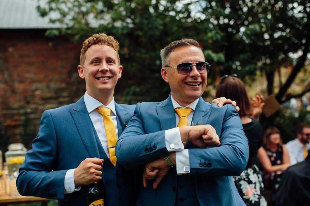 Groomsmen in coordinated blue suits and yellow accessories sharing laughs at an outdoor event.