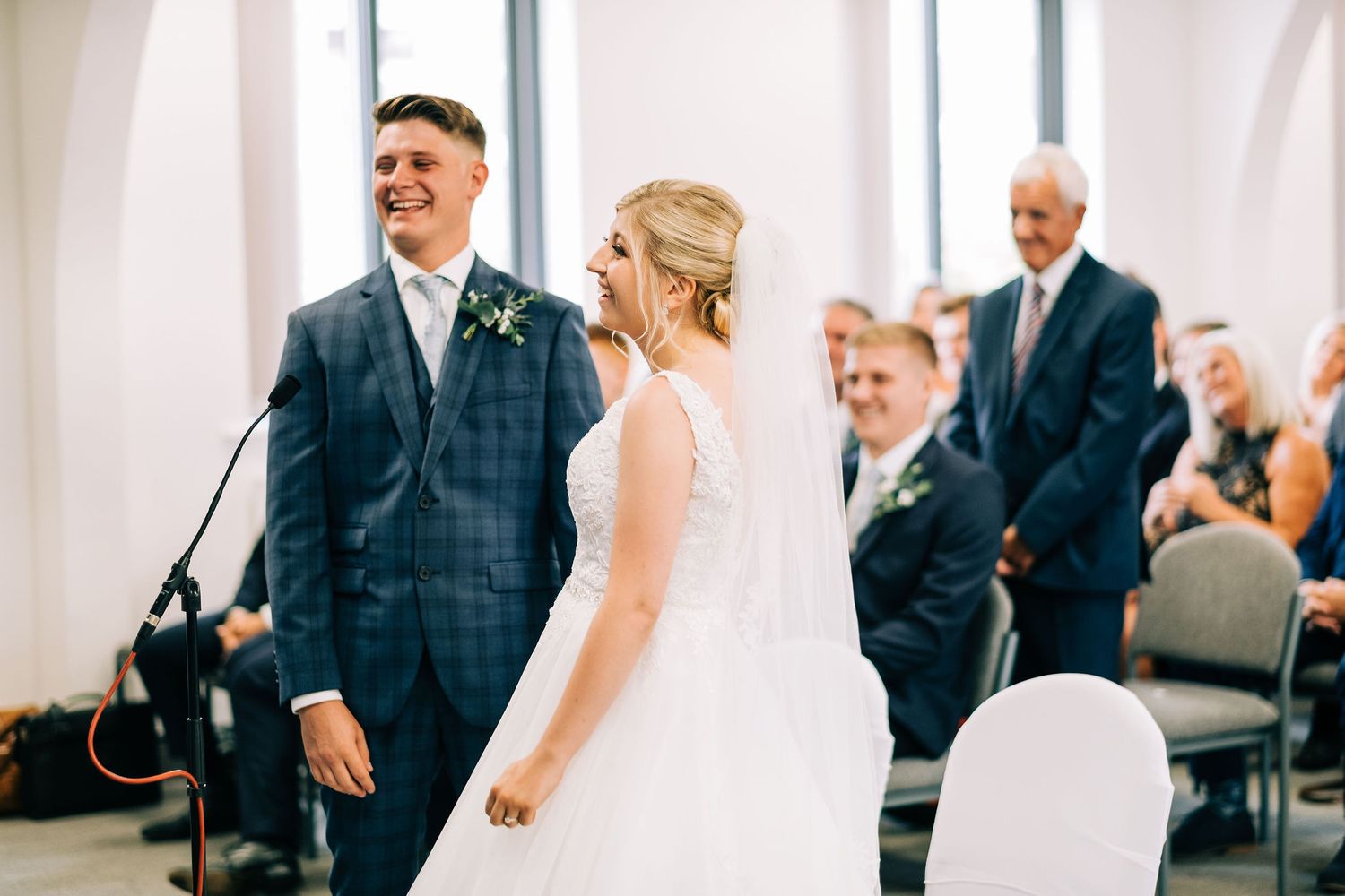 Indoor wedding ceremony with guests seated in white chairs watching the couple exchange vows.