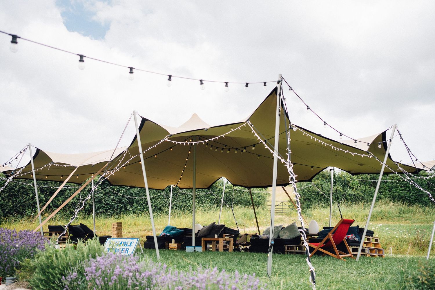 Rustic outdoor wedding tent with fairy lights and bunting in a green meadow setting.