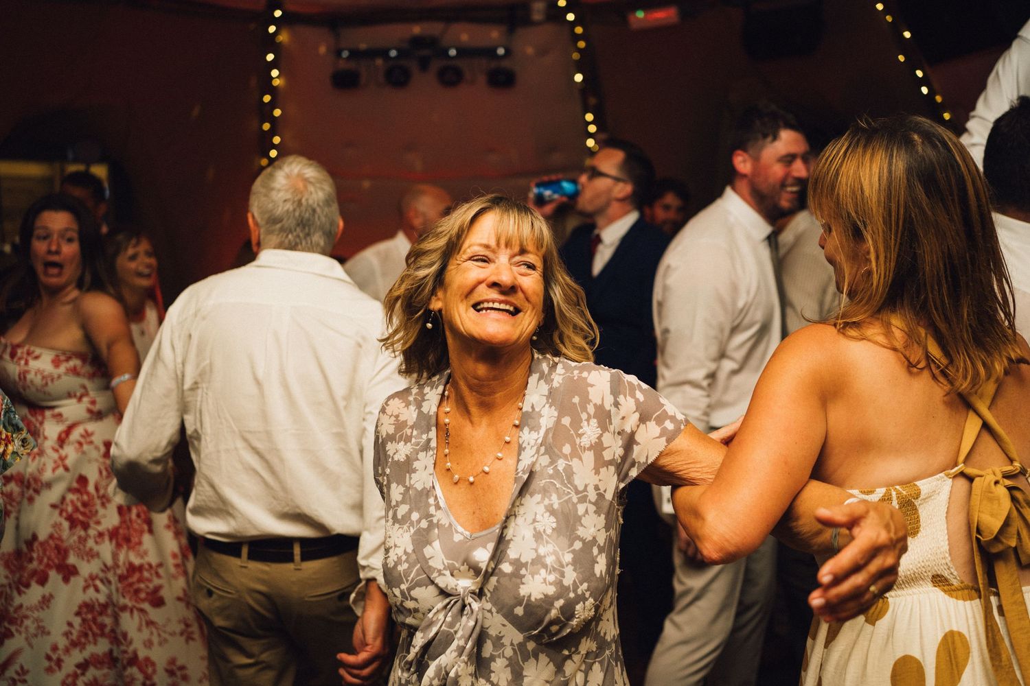Wedding reception party with guests dancing and celebrating under warm lighting and decorative string lights.
