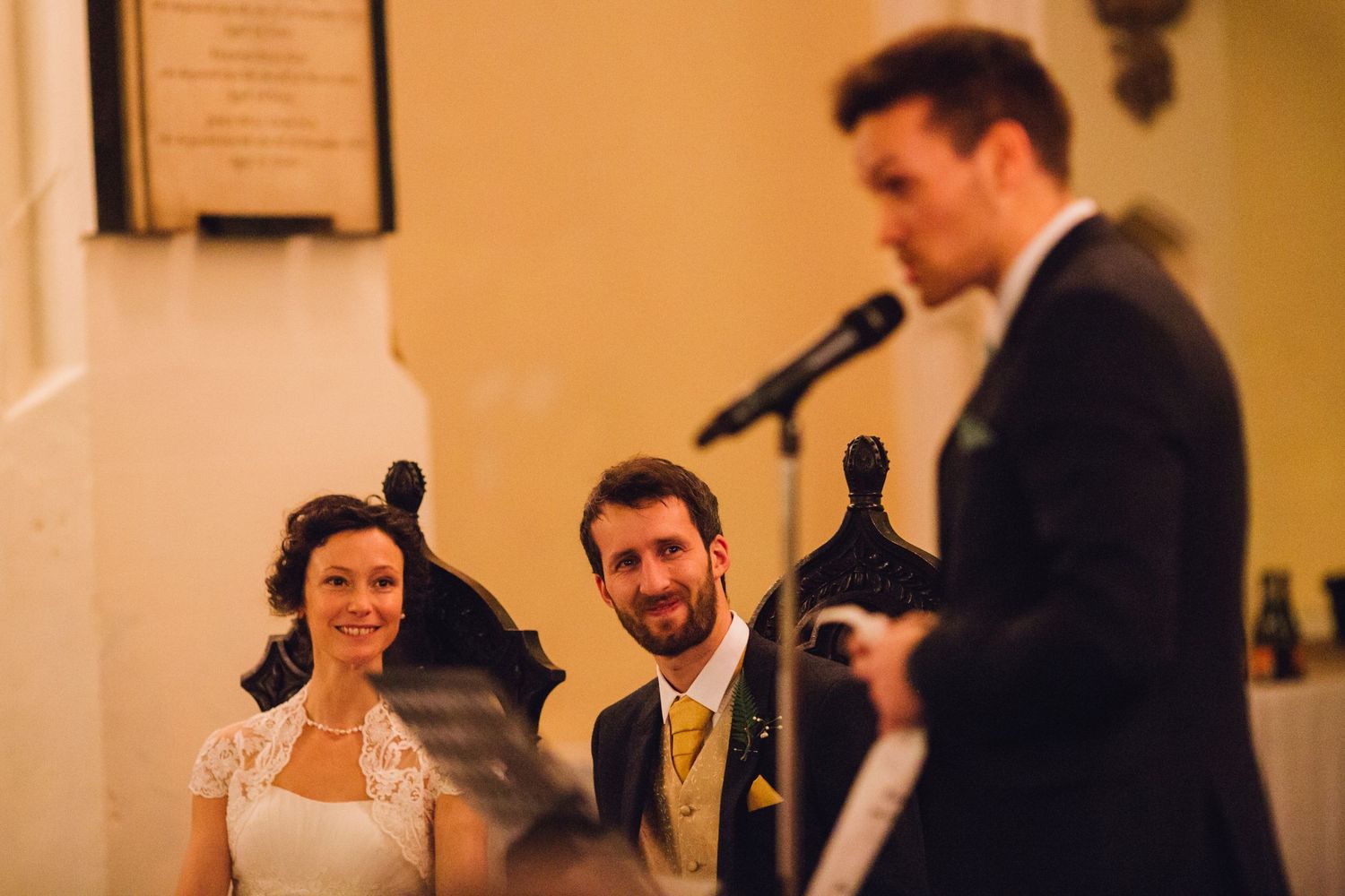 Wedding guests enjoying speeches and toasts during an elegant indoor reception celebration.