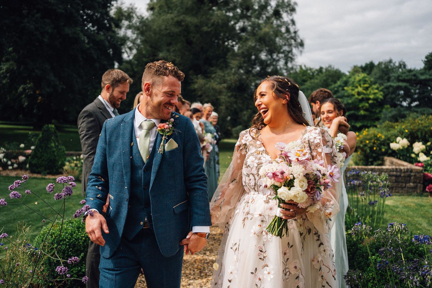 A couple walks together and laughs on their wedding day in a garden setting.