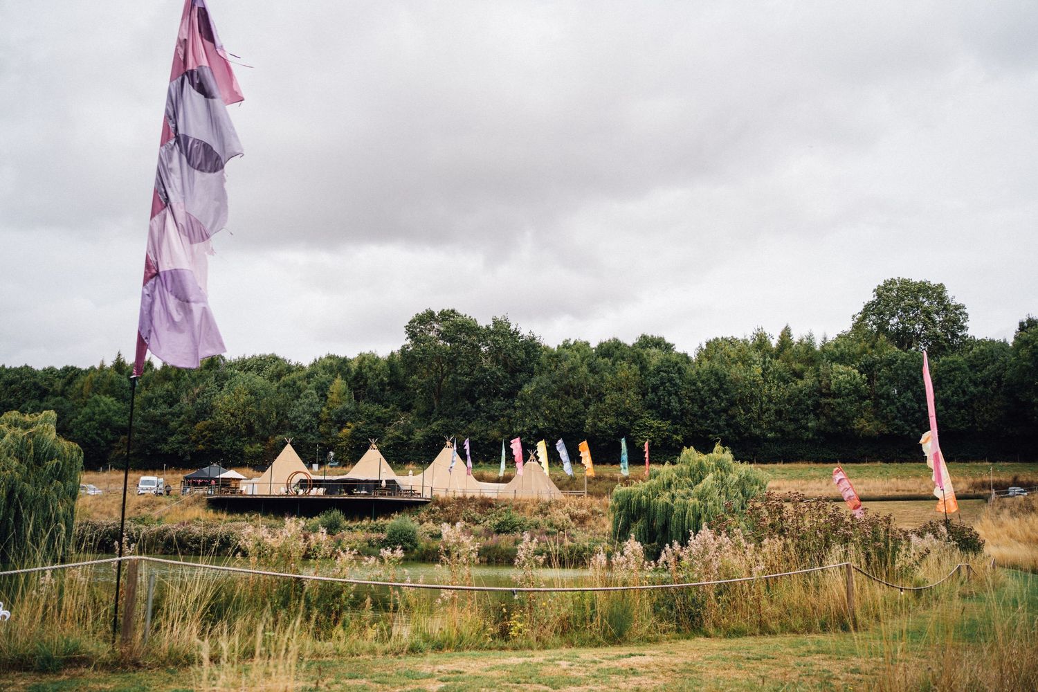 Row of white glamping tents set up in a grassy field with colorful flags flying above.