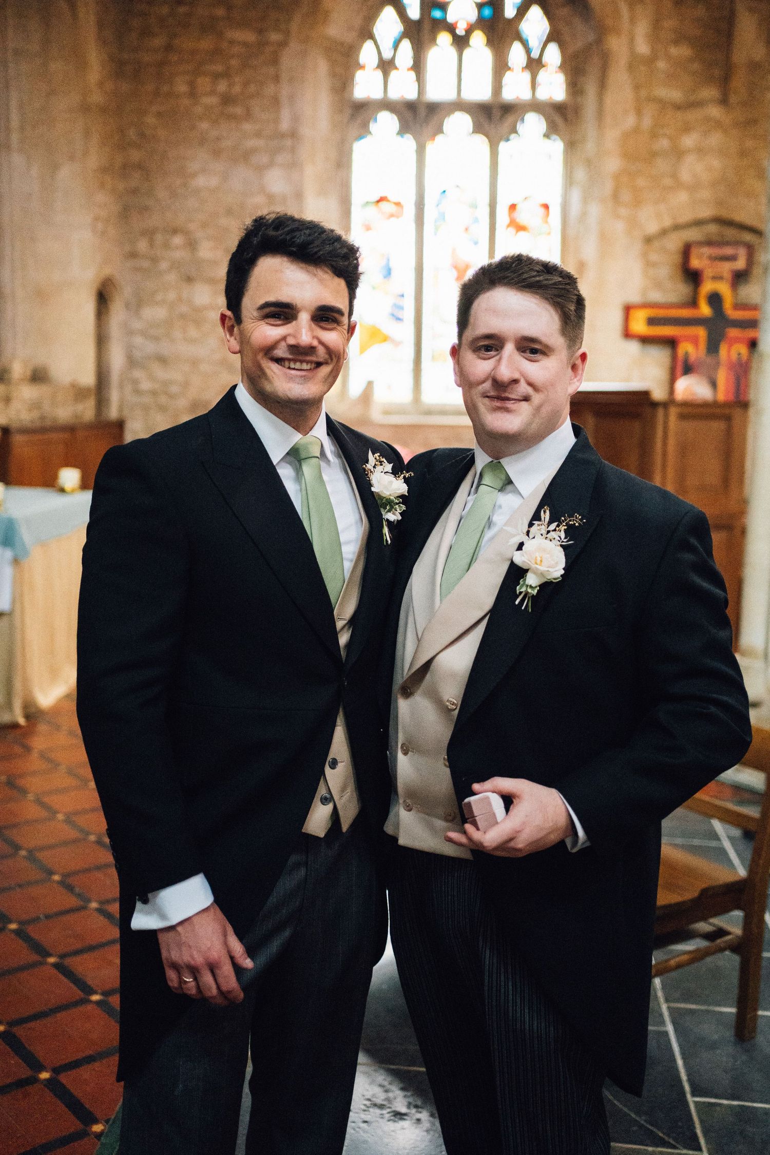 Wedding party members in formal attire standing inside historic church with stained glass windows.