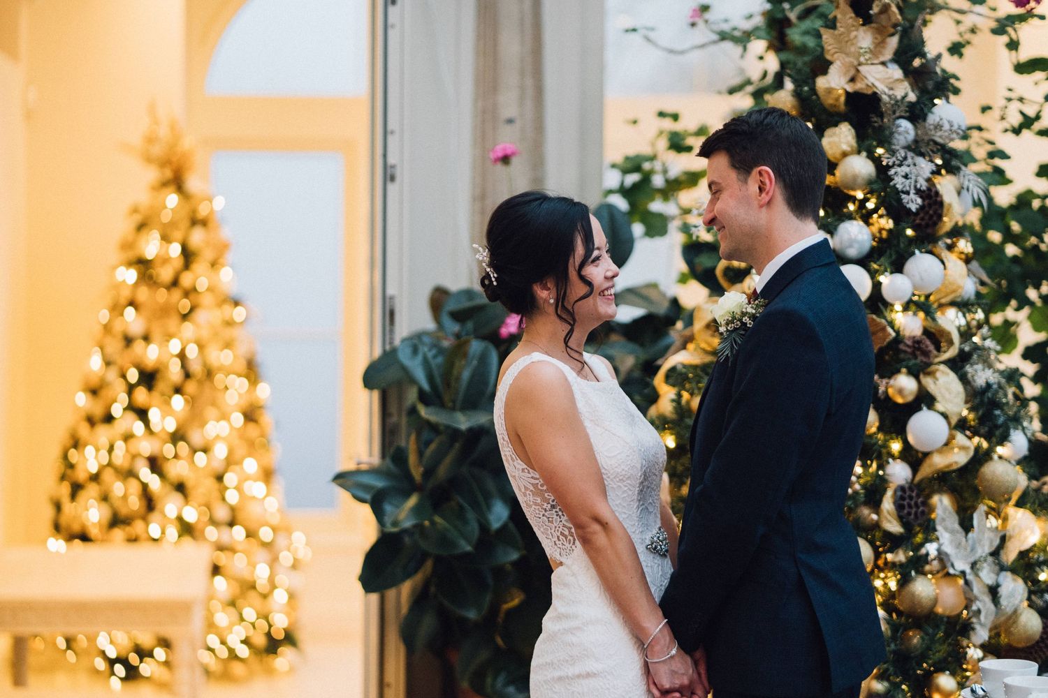 Wedding couple photographed against warm glowing Christmas trees and floral arrangements.