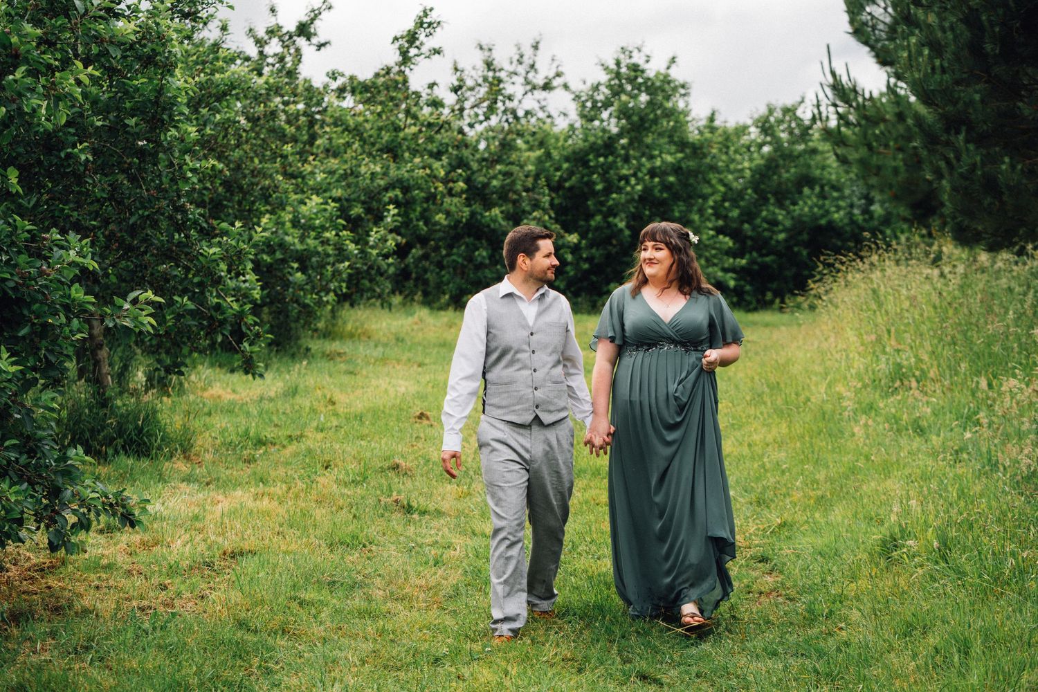 Two people strolling through a verdant garden path surrounded by leafy green bushes.