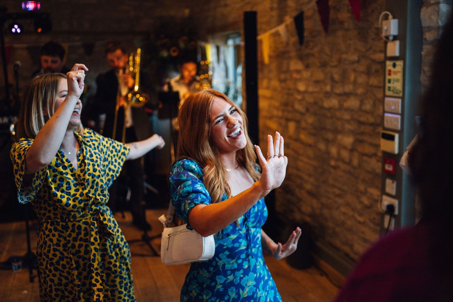 Wedding party dancing and celebrating in a dimly lit venue with brick walls.