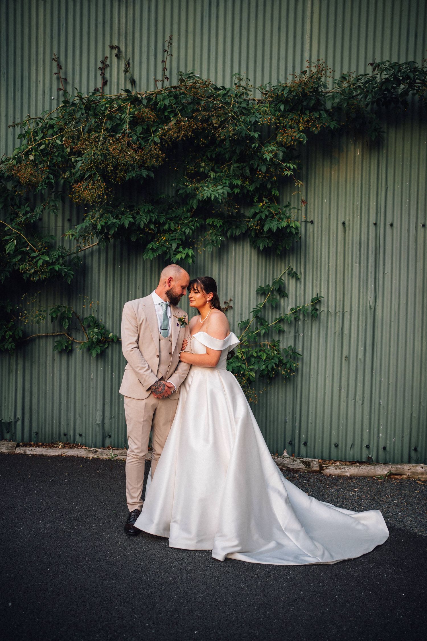 A couple shares an intimate moment against a corrugated metal wall with ivy, captured in a series of romantic wedding photos.