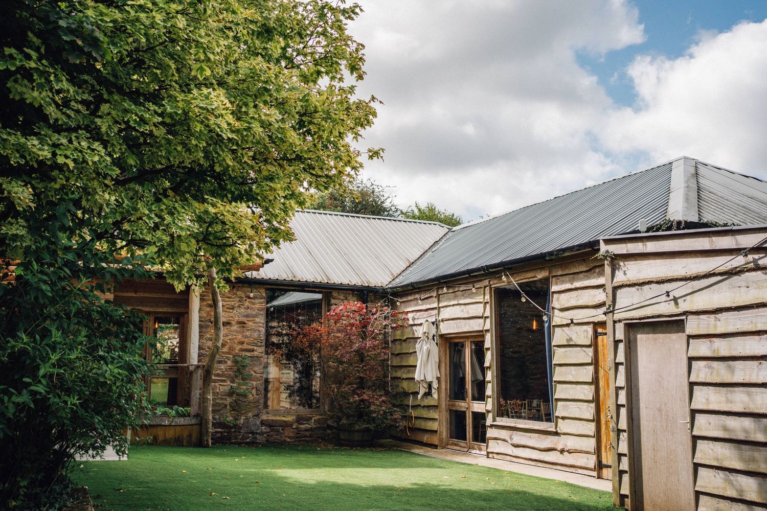 Rustic log cabin style venue exterior with green landscaping and cloudy sky.