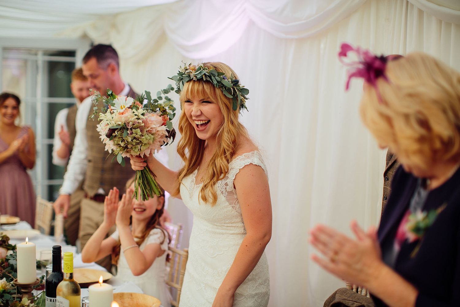 Wedding reception guests celebrating in a white draped tent with floral decorations.