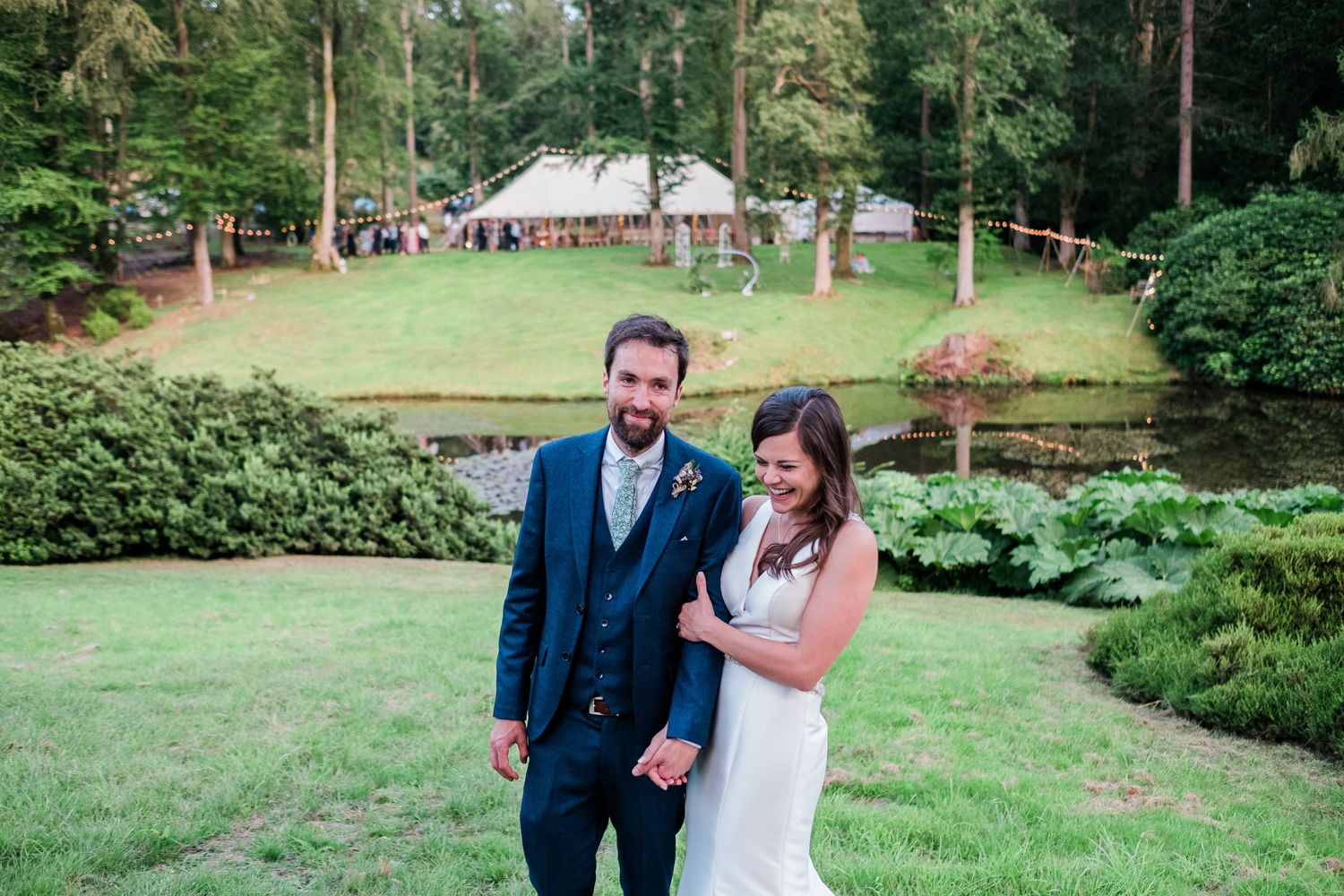 Wedding couple poses for portraits in a scenic garden with tall trees and green lawns.