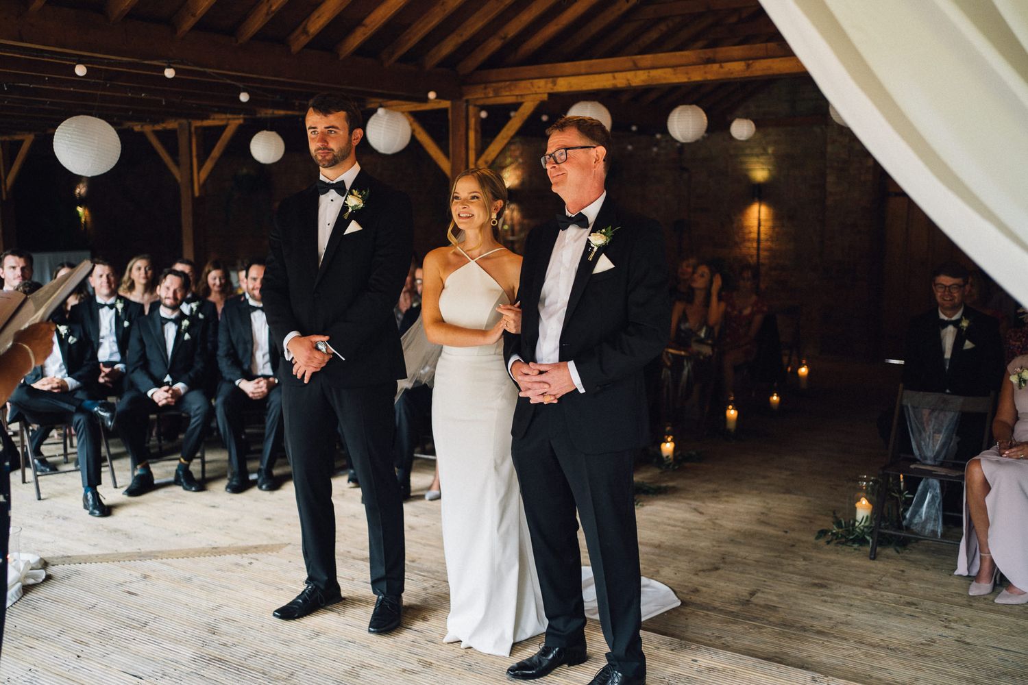 Wedding celebration captured in panoramic view showing rustic barn interior with elegant lighting and decor.