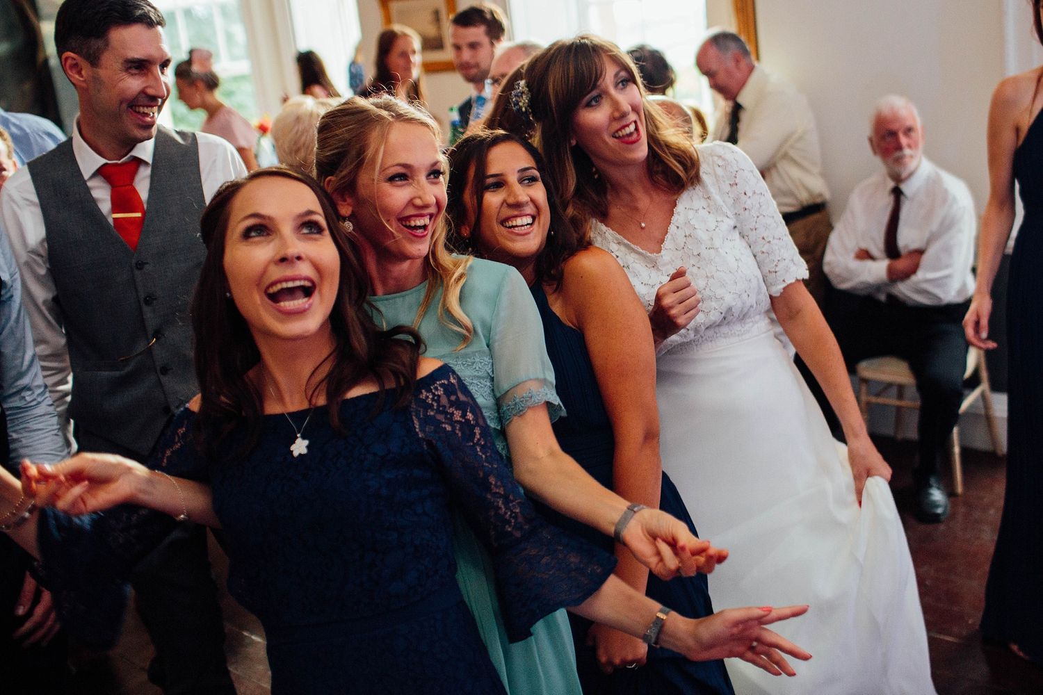 Joyful wedding celebration with guests dancing and laughing in formal attire.