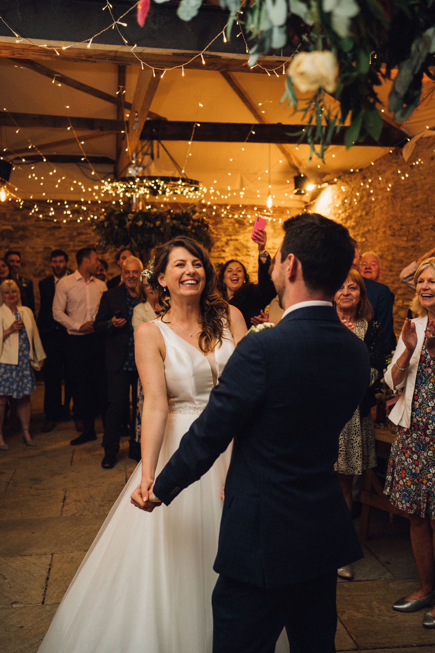 Wedding couple dancing under twinkling lights at rustic indoor reception.