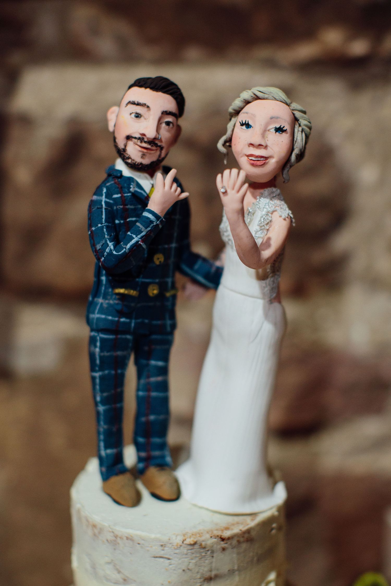 Custom wedding cake toppers showing miniature figures in navy suit and white dress.