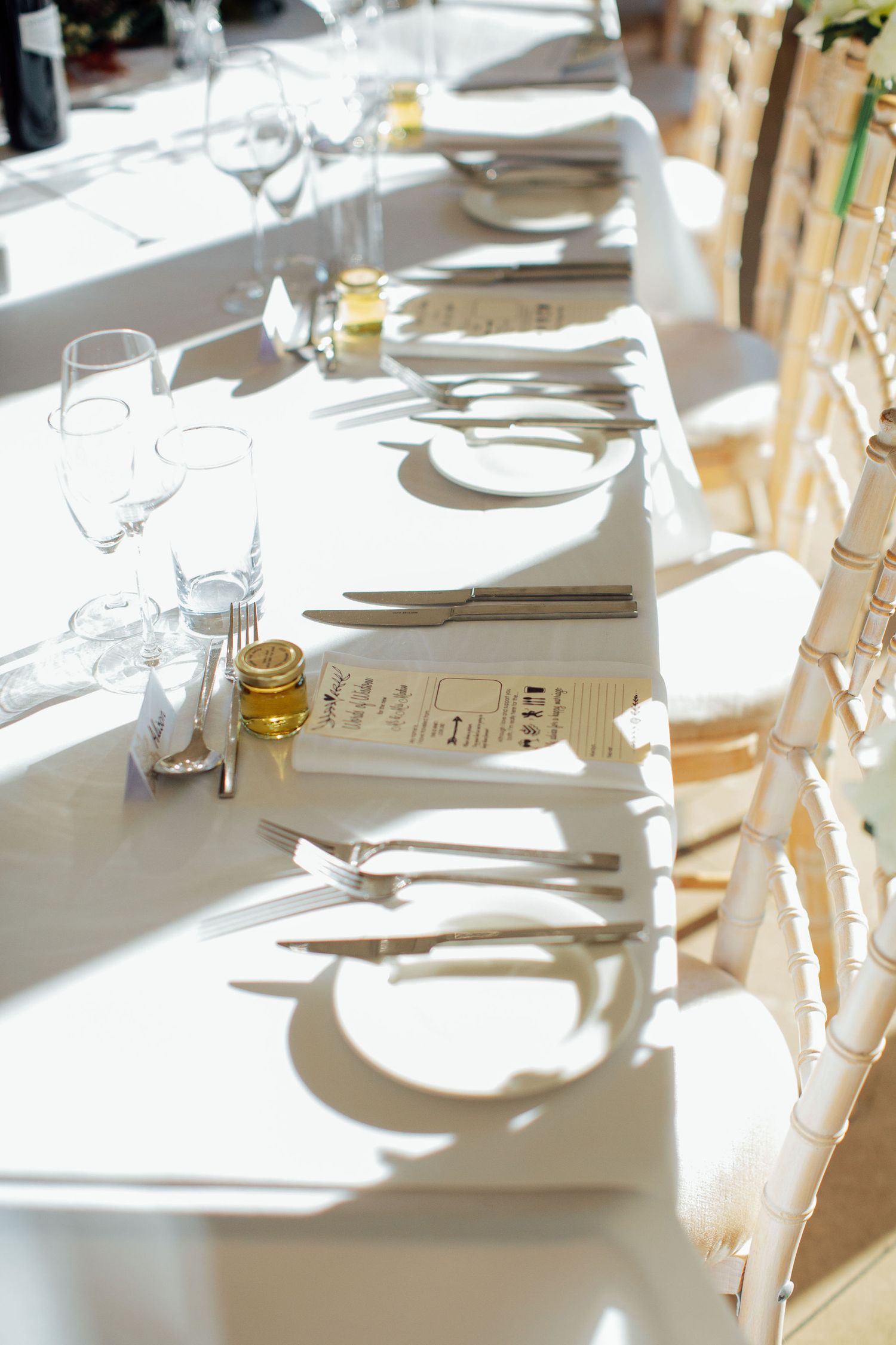 Elegant table settings with white linens and glassware casting shadows in natural sunlight.