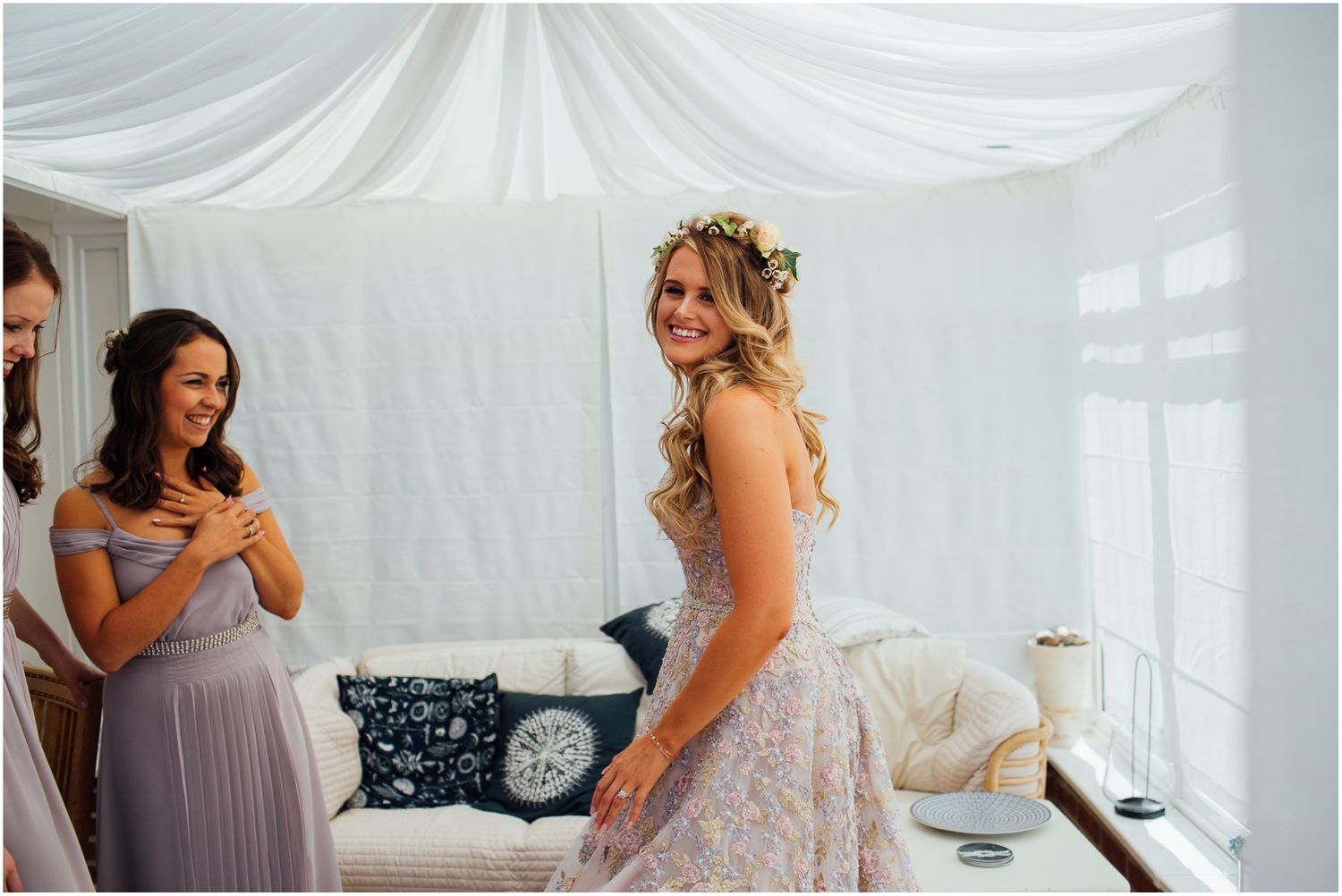 Bridal party reacts with excitement in a white draped room with elegant decor.