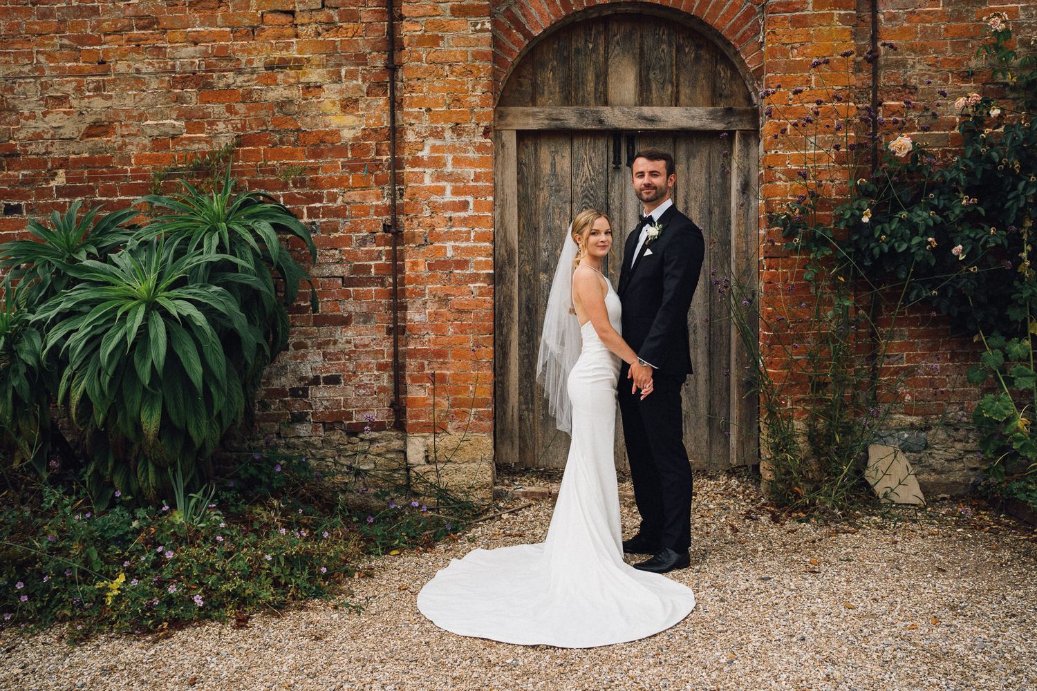 Elegant wedding portraits taken against rustic brick wall backdrop with garden elements.