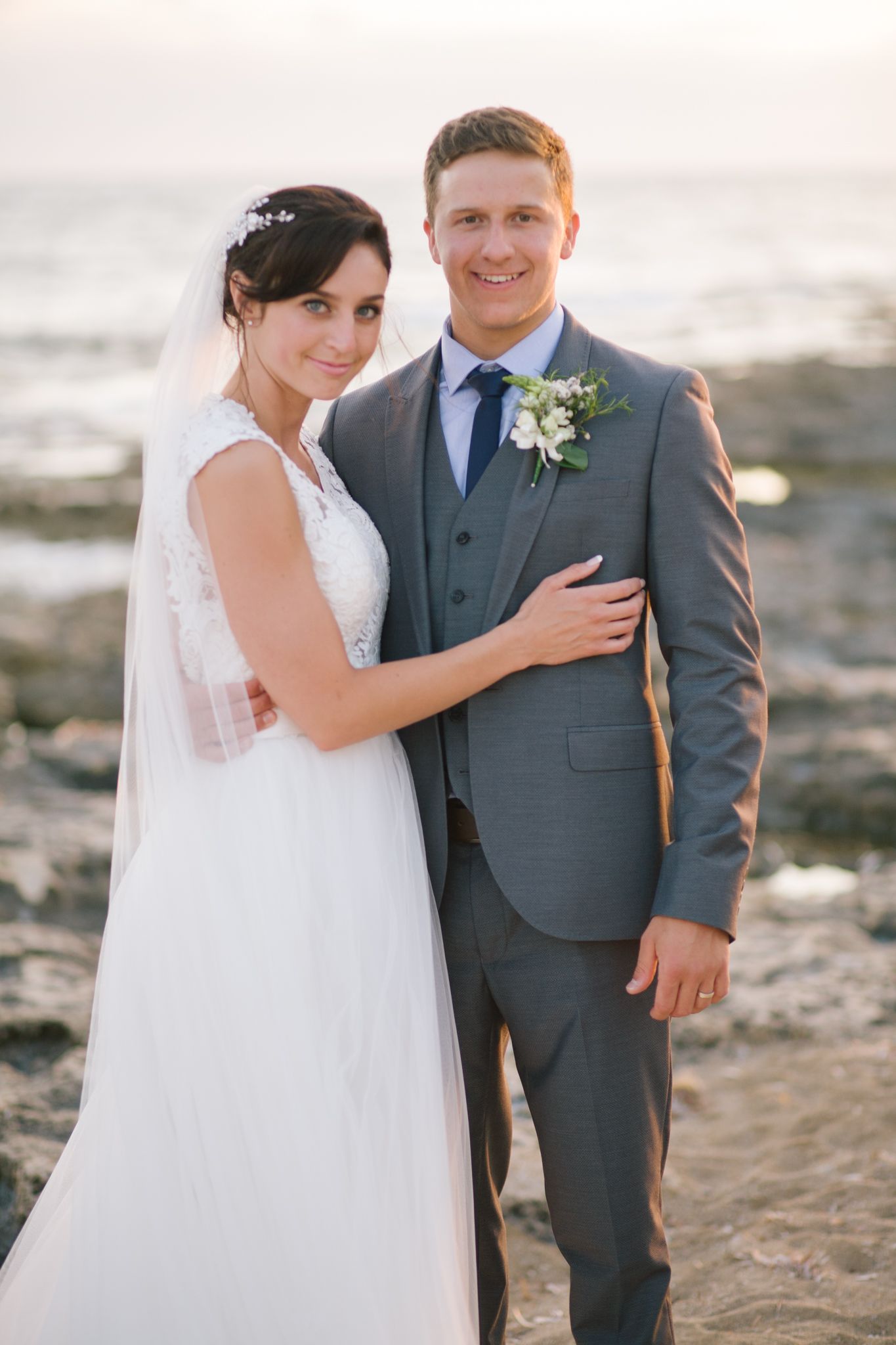 A romantic seaside portrait of newlyweds in formal wedding attire against an ocean backdrop.