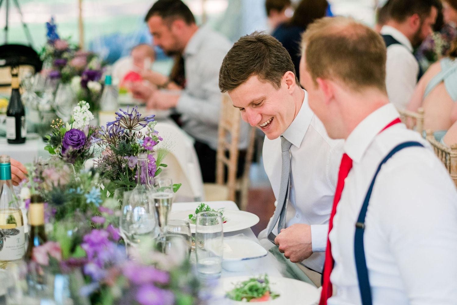 Wedding reception table settings with purple floral centerpieces and formal place settings.