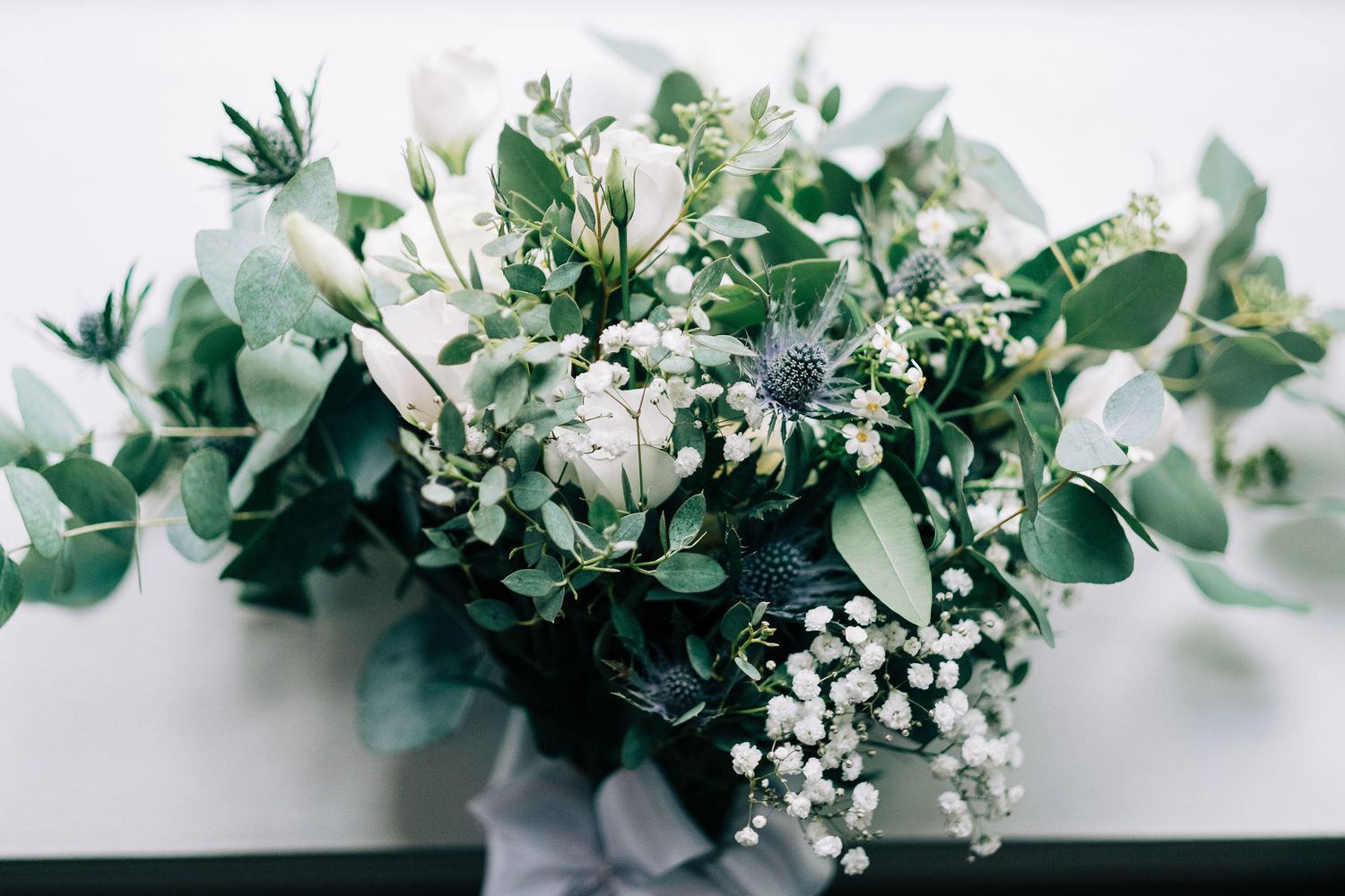 Delicate white floral arrangements with eucalyptus leaves and baby's breath displayed against a light background.