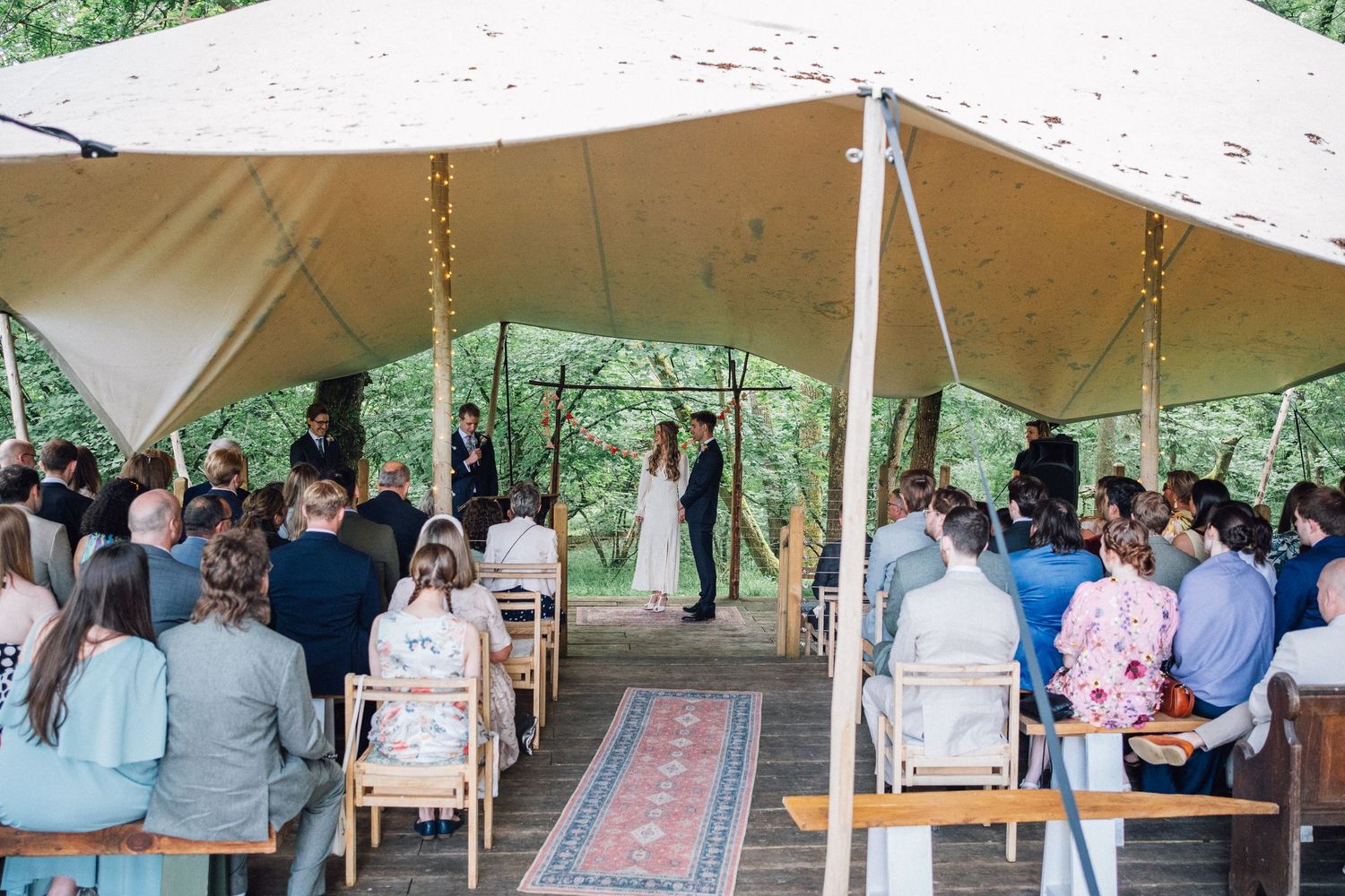 Outdoor wedding ceremony and reception setup with white tent canopies and rustic decor in a garden setting.