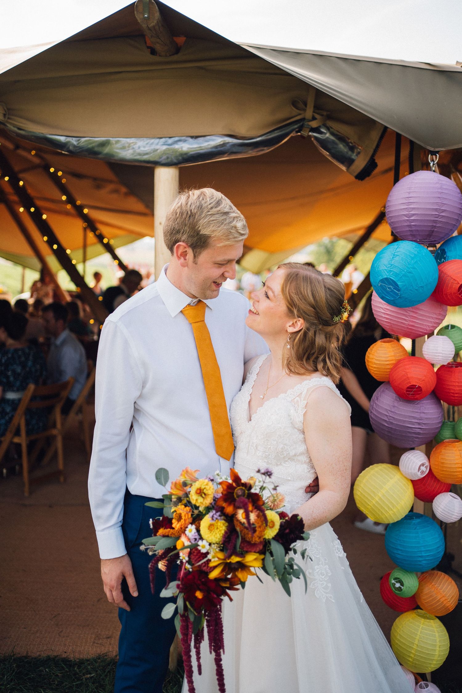 A couple shares romantic moments under colorful paper lanterns at an outdoor wedding reception.