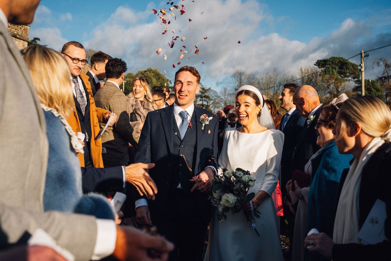 Wedding guests celebrate outdoors as pink confetti falls through the air during a joyful reception moment.