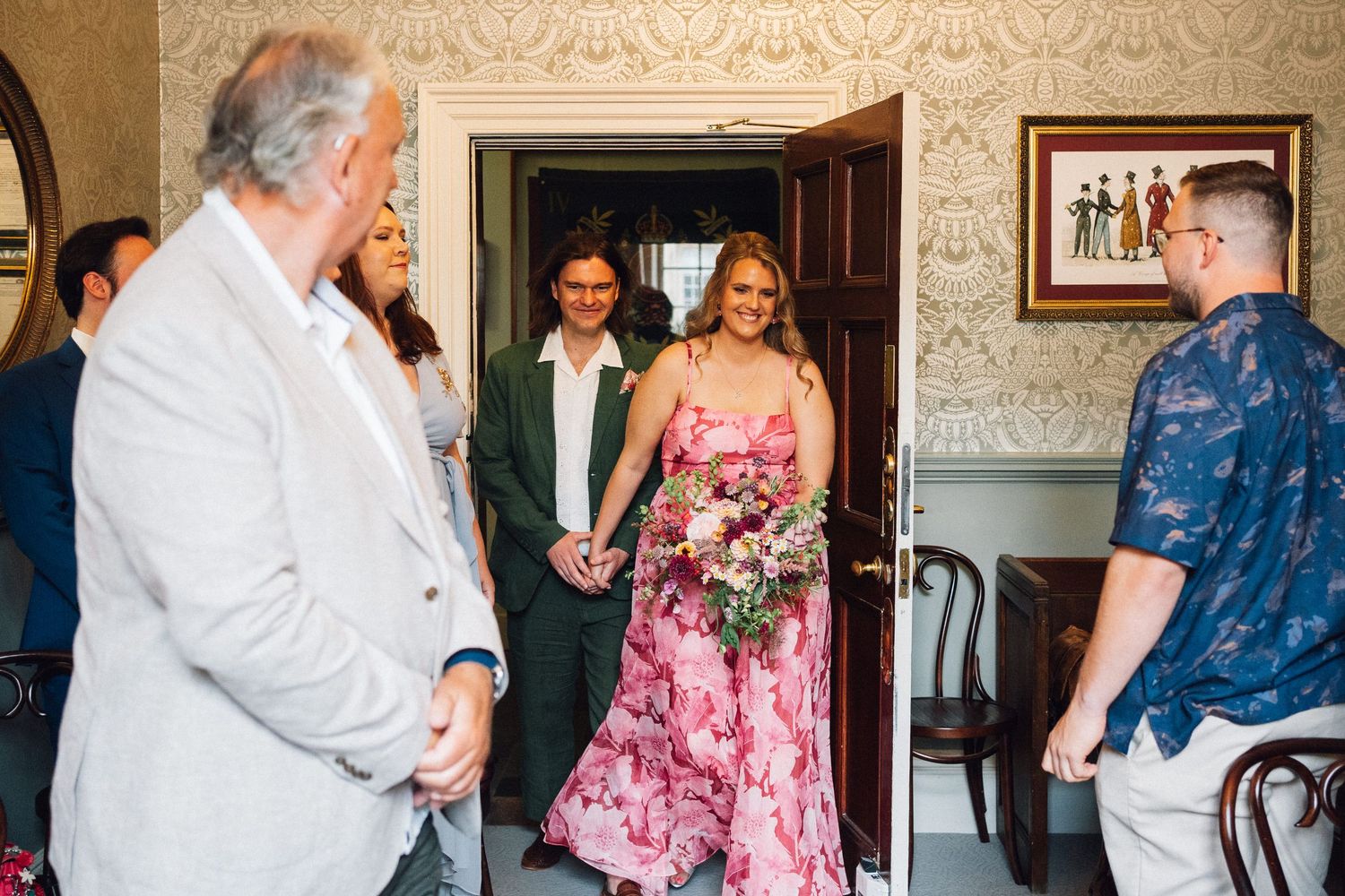 Wedding guests gather in an elegant room with ornate wallpaper and traditional decor.