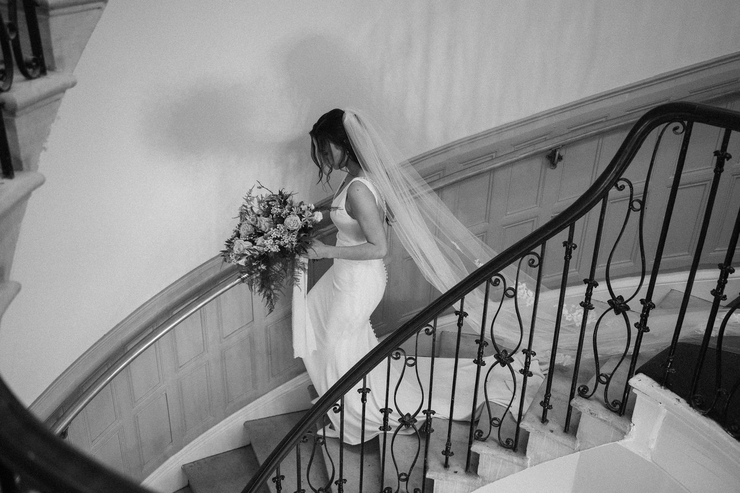 A black and white photo series showing a person descending a spiral staircase with wrought iron railings.