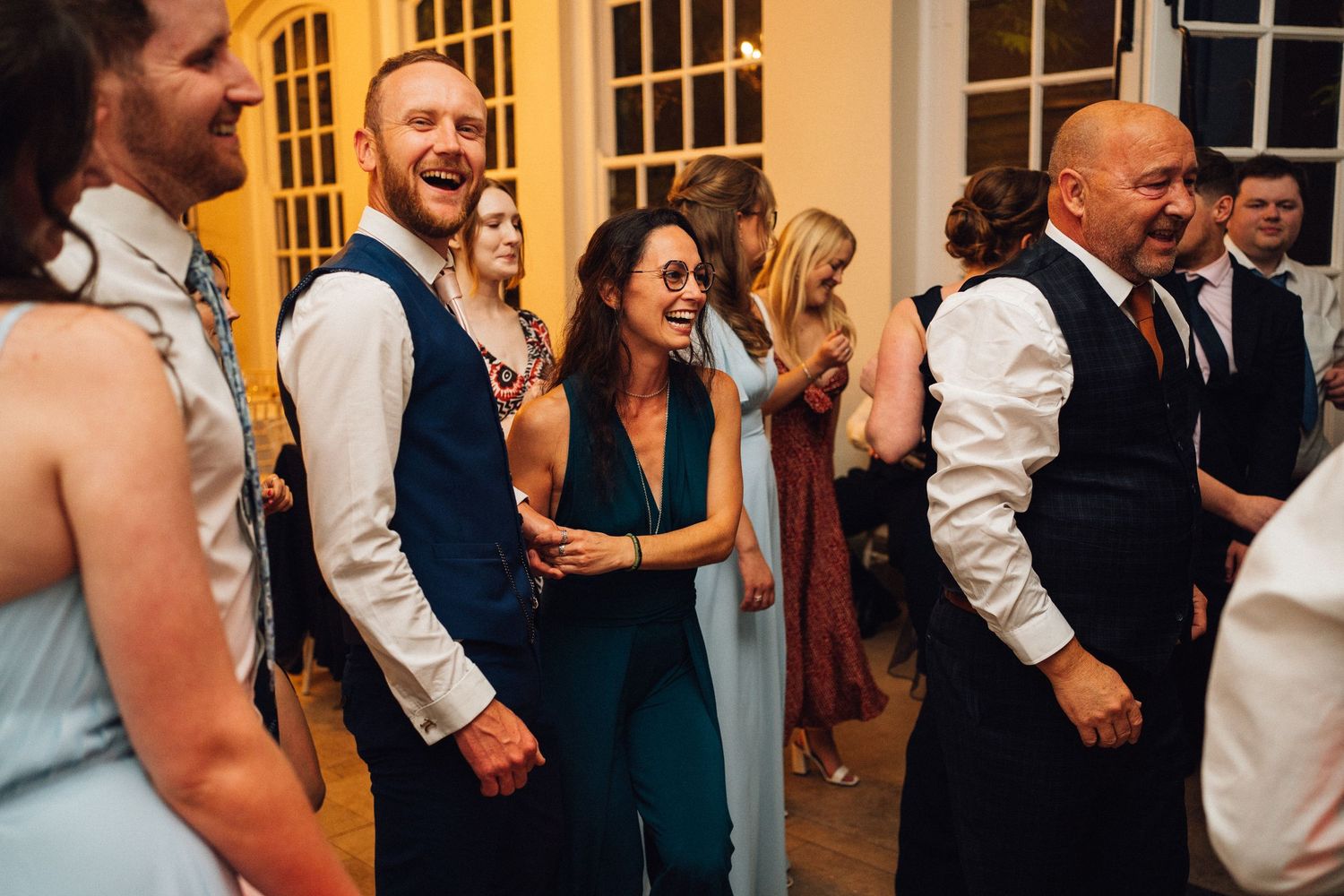 Wedding guests dancing and celebrating together on a crowded dance floor at an elegant indoor reception venue.
