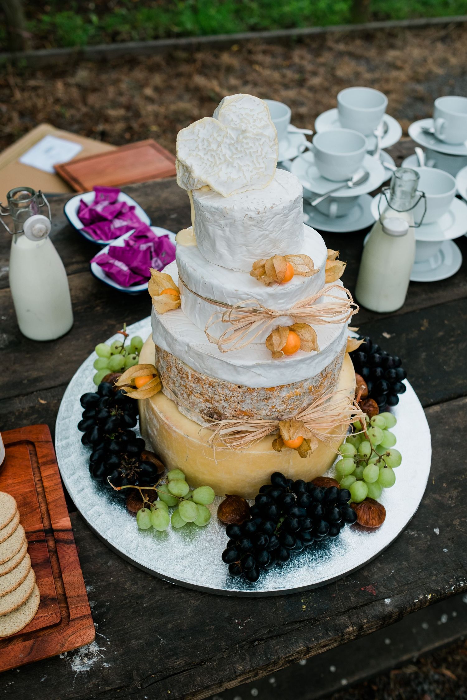 Elegant cheese wheel wedding cake decorated with fresh grapes and flowers on a rustic wooden surface.