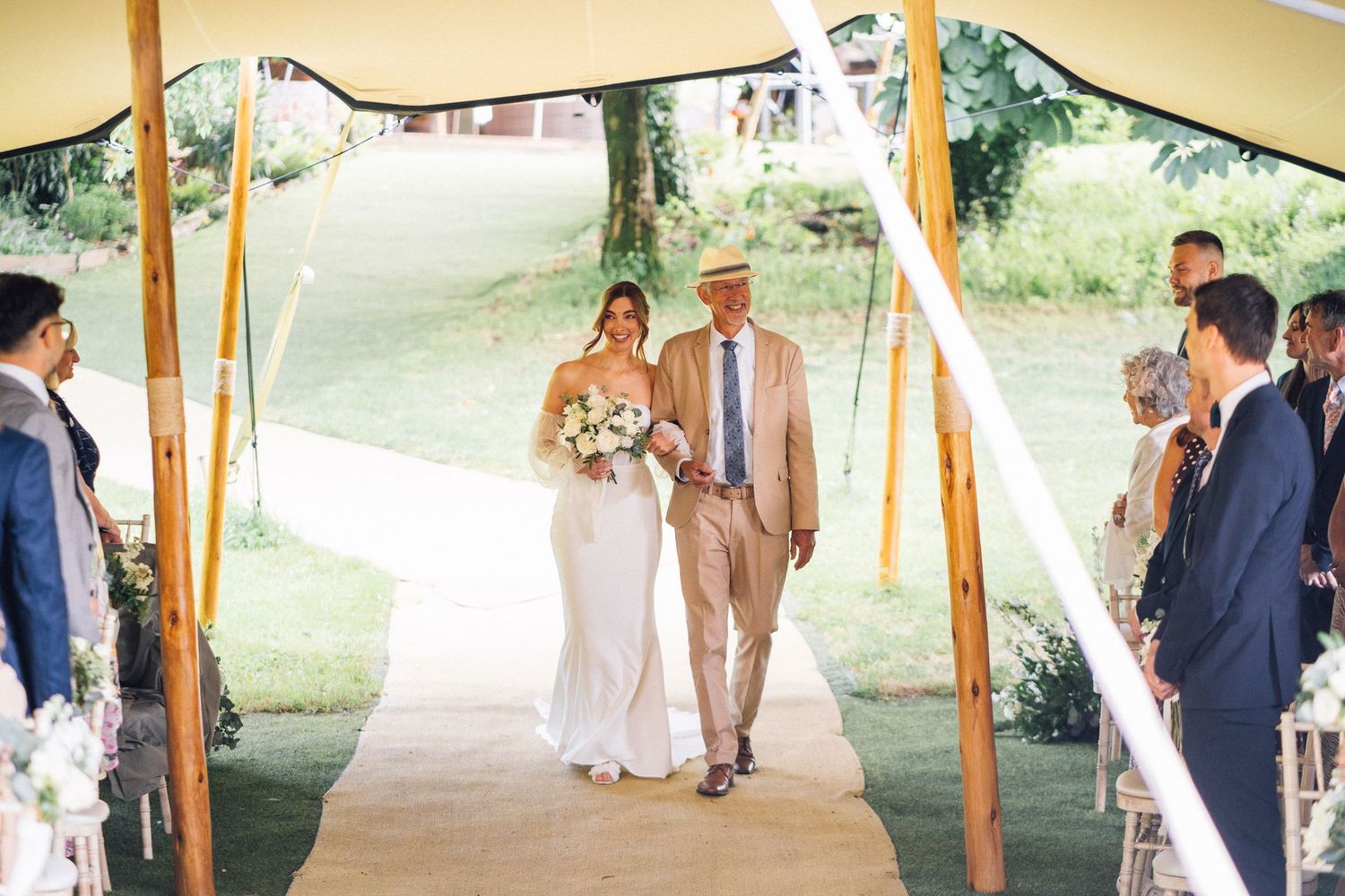 Wedding party walking and celebrating under outdoor tent canopy on sunny day.