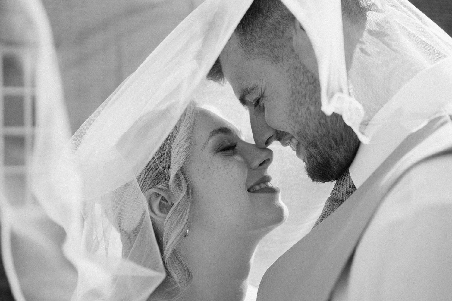 Intimate black and white portrait of newlyweds sharing a tender moment under the bride's veil.