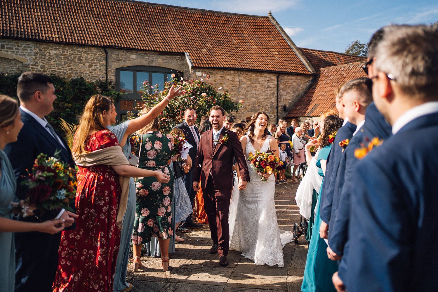Wedding guests gather outside a rustic brick barn venue during a sunny outdoor celebration.