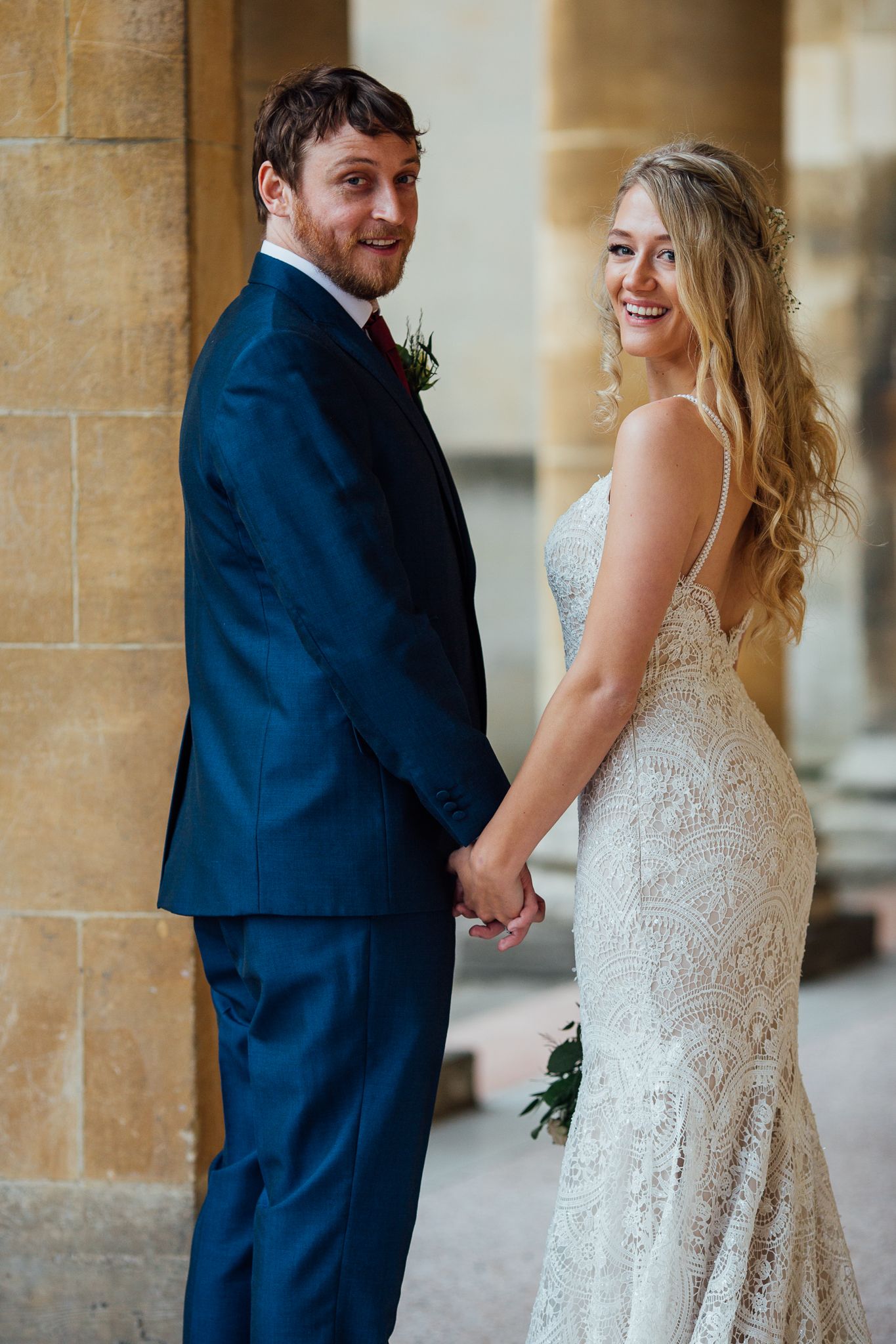 A couple in wedding attire poses together against a stone building on their special day.