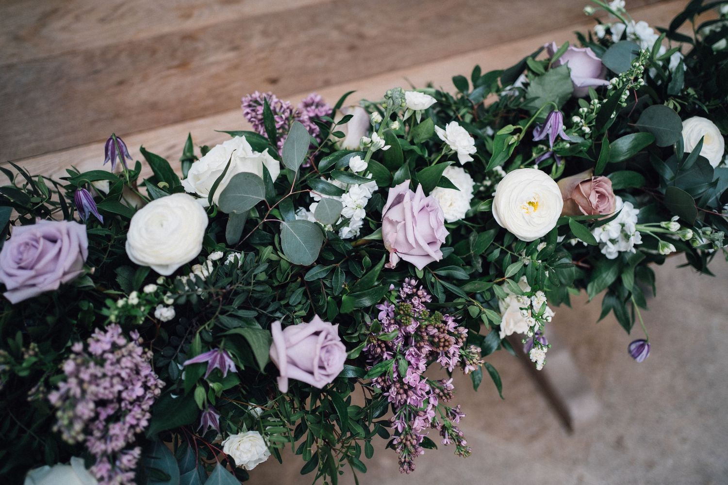 Floral garland with white roses, lavender blooms, and greenery decorating a wedding venue space.
