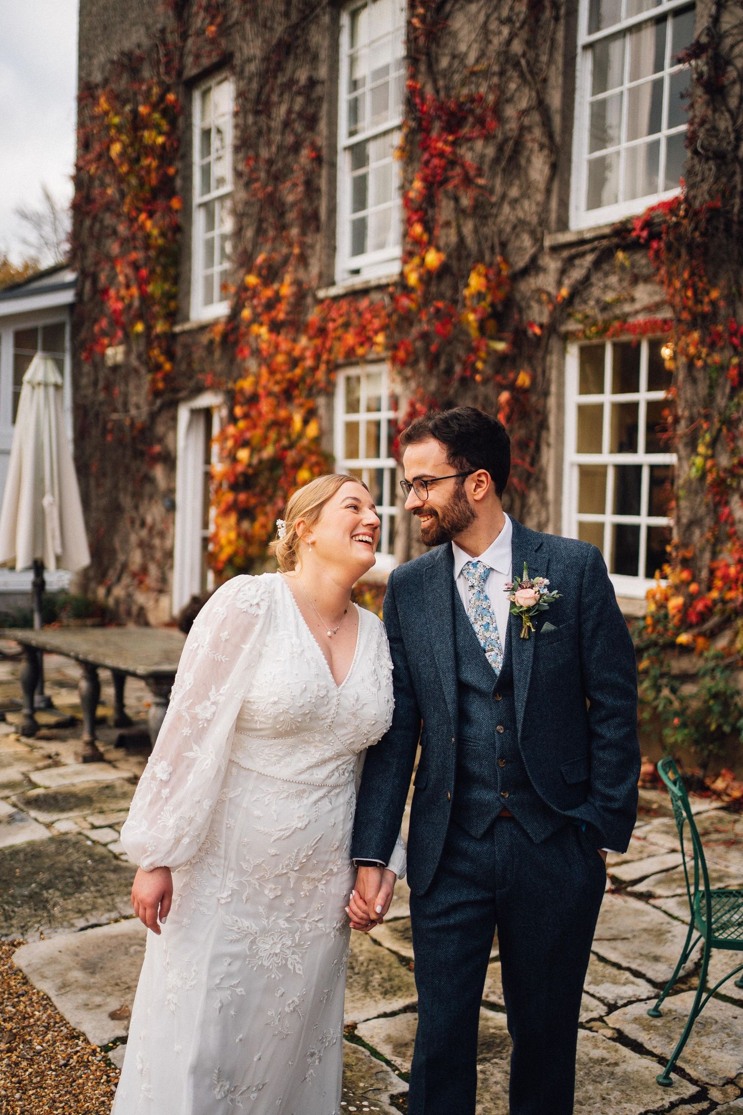 A couple shares a joyful moment on their wedding day outside a stone building with vibrant autumn ivy.