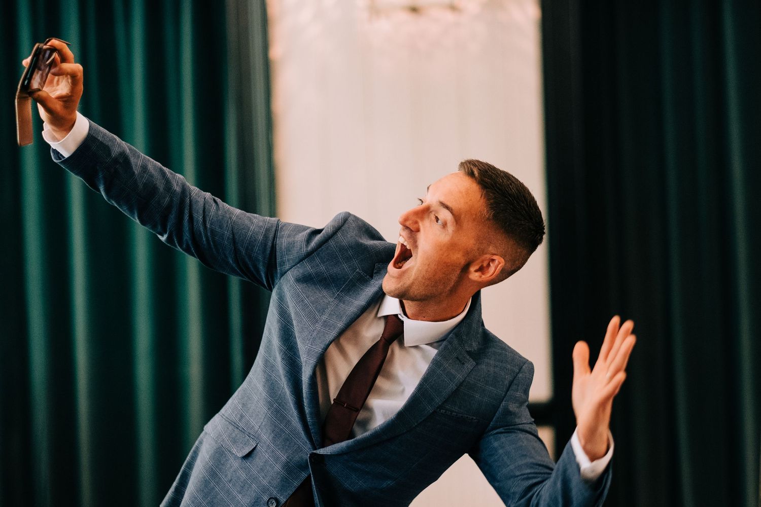 Wedding guests dancing and celebrating at an indoor reception with dark curtains.